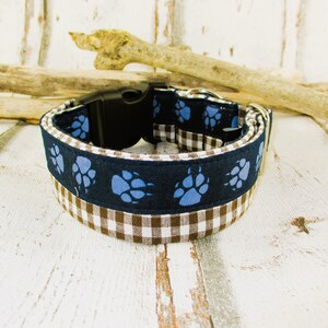 Könnte beinhalten: Ein braunes und weißes Gingham-Hundehalsband mit einem blauen Pfotenabdruckmuster. Das Halsband hat eine schwarze Kunststoffschnalle.
