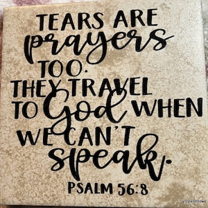 May include: A beige square tile with black lettering that reads "Tears are prayers too. They travel to God when we can't speak. Psalm 56:8".