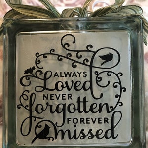May include: A glass block with a black vinyl decal that reads "Always Loved Never Forgotten Forever Missed". The decal features a stylized floral design and two birds.