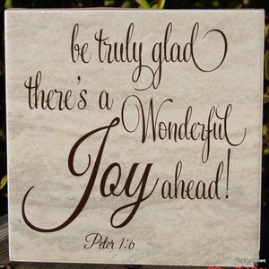 May include: A beige tile with brown lettering that reads "be truly glad, there's a wonderful joy ahead!" with the scripture reference "Peter 1:6" below.