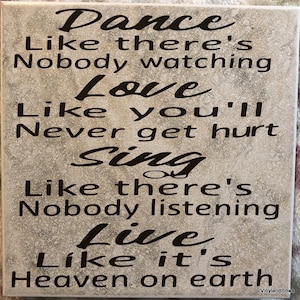 May include: A decorative tile with a gray background and black text that reads "Dance like there's nobody watching, Love like you'll never get hurt, Sing like there's nobody listening, Live like it's heaven on earth".