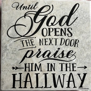 May include: A gray stone sign with black lettering that reads "Until God opens the next door praise Him in the hallway".