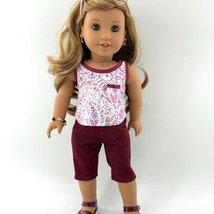 Può includere: Una bambola con lunghi capelli castano chiaro che indossa occhiali da sole bianchi sulla testa, un top senza maniche con motivo paisley rosa e bianco, pantaloni capri bordeaux scuro e sandali bordeaux abbinati. Indossa piccoli orecchini.