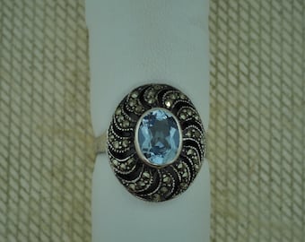 May include: A silver ring with a blue oval gemstone surrounded by a detailed design of marcasite stones.