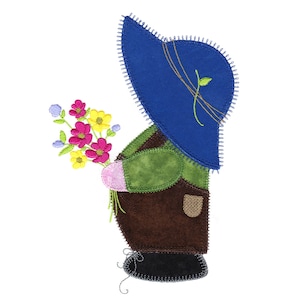 Könnte beinhalten: Eine blaue und braune Patchworkpuppe mit einem blauen Hut und einem Strauß rosa, gelber und lila Blumen.