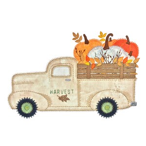 May include: A white vintage pickup truck with the word "HARVEST" on the side, carrying a bed full of orange and white pumpkins with fall leaves.