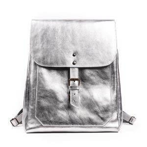 May include: A silver leather backpack with a buckle closure and a flap pocket.