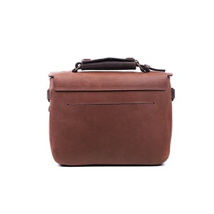 May include: A brown leather satchel bag with a top handle and a flap closure. The bag has a front pocket and a back pocket. The bag is made of high-quality leather and has a classic design.