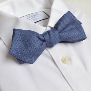 May include: A blue bow tie made of a textured fabric, worn on a white dress shirt.