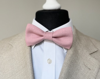 May include: A light pink linen bow tie on a white shirt and a beige herringbone blazer.