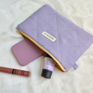 May include: A lavender quilted cosmetic bag with a gold zipper, containing a lavender phone, hand cream, and a tube of lip gloss. The bag has a small label that reads "ADATELE".