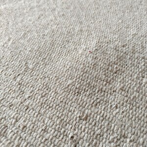 May include: Close-up of a textured, off-white woven fabric. The weave is tight, creating a slightly ridged surface. The fabric appears to be made of natural fibers, with subtle variations in color and texture. The overall look is neutral and organic.