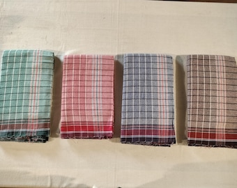 May include: Four folded rectangular towels in a row. Each towel has a plaid pattern with a different color scheme: green, red, blue, and brown. The towels have a fringed edge.