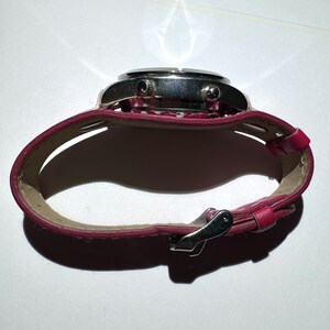 May include: A silver wristwatch with a red leather band. The band has a white polka dot pattern. The watch has a silver buckle.