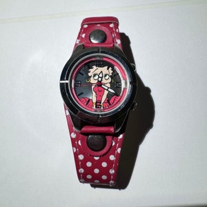 May include: A red and white polka dot wristwatch with a silver face featuring a cartoon image of Betty Boop.