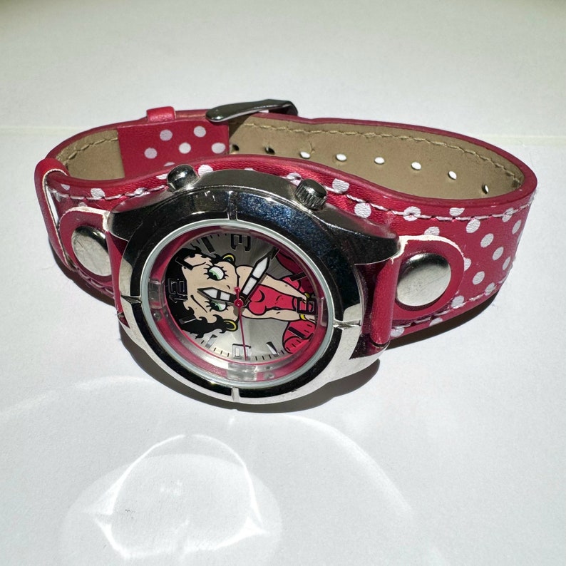 May include: A red and white polka dot watch with a silver band and a cartoon image of Betty Boop on the face.
