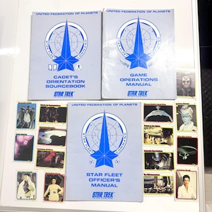 May include: Three Star Trek manuals and trading cards are displayed. The manuals are light blue with a blue starburst design and the text "United Federation of Planets" and "Star Fleet Command". The manuals are titled "Cadet's Orientation Sourcebook", "Game Operations Manual", and "Star Fleet Officer's Manual".