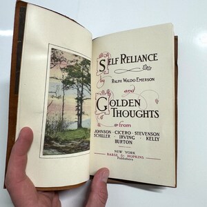 K&ouml;nnte beinhalten: Ein ge&ouml;ffnetes Buch mit braunem Lederumschlag. Die Titelseite ist sichtbar und lautet "Self Reliance by Ralph Waldo Emerson and Golden Thoughts from Johnson, Cicero, Stevenson, Schiller, Irving, Burton, Kelly". Das Buch wurde von Barse & Hopkins in New York ver&ouml;ffentlicht.