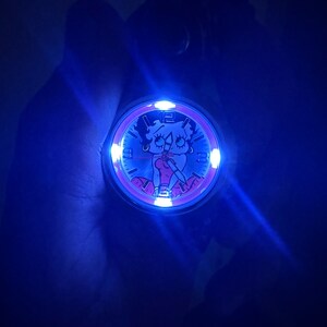 May include: A pink and silver watch with a cartoon character on the face. The watch is illuminated with a blue light.