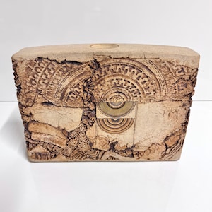 May include: A rectangular ceramic vase with a textured surface and geometric patterns in brown and white. The vase has a rough, rustic look and is perfect for displaying flowers or other decorative items.