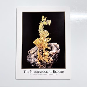 May include: A magazine cover featuring a detailed image of a golden mineral formation on a rock against a black background. The magazine title "The Mineralogical Record" is displayed at the bottom, along with the issue details.