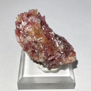 May include: A cluster of pink and brown crystals on a white display stand. The crystals are translucent and have a rough, irregular surface.