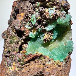 May include: A close-up of a green and brown mineral specimen. The green mineral is in a cluster of small crystals, and the brown mineral is in a rough, textured matrix.
