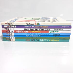 May include: A stack of colorful children's books with titles including "Dr. Seuss's ABC", "Elephant Joe, Brave Firefighter!", and "Put Me in the Zoo". The books have various colored spines and are stacked on top of each other.
