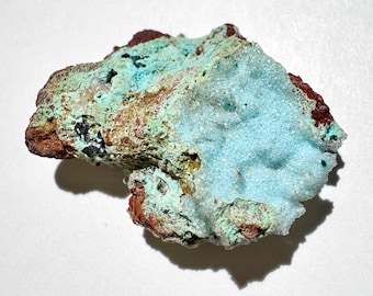 May include: A close-up of a mineral specimen with a rough, irregular shape. The mineral features a mix of colors, including light blue, turquoise, brown, and dark red. The texture appears crystalline and porous, with a matte finish.