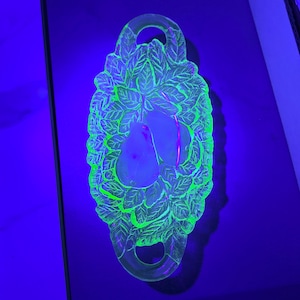 May include: A green glass serving dish with a pear design. The dish has two handles and is made of uranium glass, which glows under a black light.