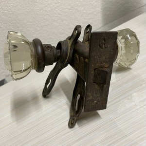 May include: Antique door knob with a brass finish and two glass knobs. The knob has a keyhole and a latch. The glass knobs are clear and have a faceted design.
