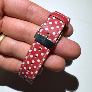 May include: Red watch strap with white polka dots and a silver buckle.