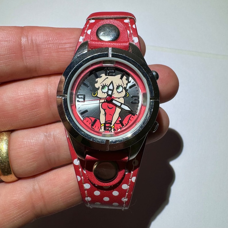 May include: Red and white polka dot wristwatch with a silver case and a cartoon image of Betty Boop on the face.