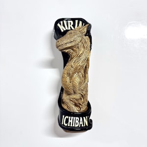 May include: A black and gold beer tap handle with a dragon design. The handle has the words "KIRIN" and "ICHIBAN" on it.