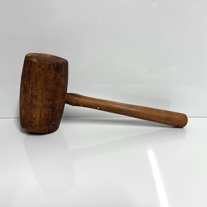 May include: A wooden mallet with a round head and a long handle. The mallet is made of dark brown wood and has a natural finish.