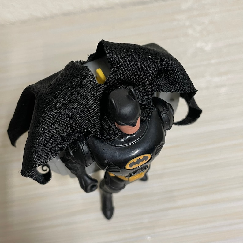 May include: Black Batman action figure with a yellow bat symbol on his chest. He is wearing a black cape and has a black and grey suit.