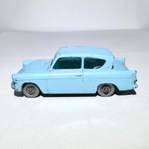 May include: A light blue toy car model of a classic Ford Anglia. The car has a detailed interior and exterior, including a windshield, wheels, and headlights.