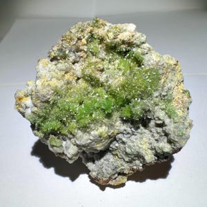 May include: A green and white mineral specimen with a rough, textured surface. The specimen is covered in small, green crystals.
