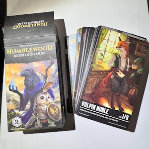 May include: A deck of Humblewood Reference Cards with a black box featuring a raven, owl, and text. The cards depict anthropomorphic animals, including a fox labeled "VULPIN NOBLE". The cards are for a tabletop role-playing game.