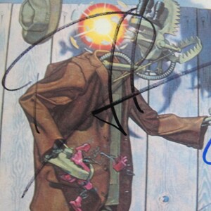 May include: A vintage record album cover featuring a robot-like figure wearing a brown jacket and a hat. The figure is holding a tool in its hand. The album cover is signed by four different people in black and blue ink.