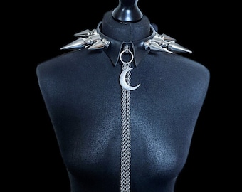 May include: Black leather choker necklace with silver-colored metal spikes and a crescent moon pendant. The necklace features a collar design with a dangling chain and moon charm, displayed on a black mannequin.