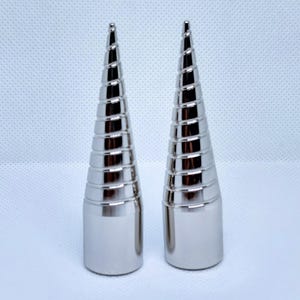 Peut inclure: Deux pointes métalliques de couleur argentée identiques avec une base cylindrique lisse et une partie supérieure conique en spirale. Chaque objet présente une série de crêtes horizontales créant une texture nervurée, se terminant par une pointe.