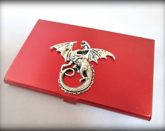 May include: A red metal business card holder with a silver dragon design.