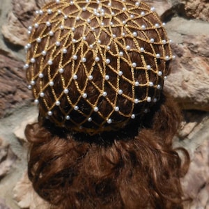 Op de afbeelding: Een gouden gaas haarnet met witte parel kralen. Het net wordt gedragen over bruin haar.