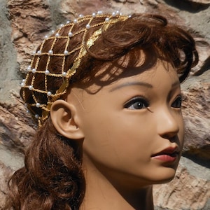 Op de afbeelding: Een gouden draad haarnet met witte parels, gedragen door een mannequin met bruin haar.