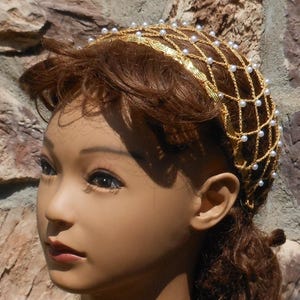 Op de afbeelding: Een gouden en witte kralen haar kroon met een net ontwerp. De kroon wordt gedragen door een mannequin met bruin haar.