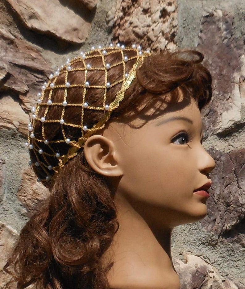 Op de afbeelding: Een gouden gaas haarnet met witte parels. Het net wordt gedragen op een mannequinhoofd met bruin haar.