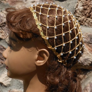 Op de afbeelding: Een gouden gehaakt haarnet met witte parel kralen. Het net wordt gedragen door een mannequin met bruin haar.