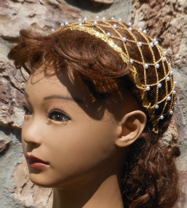 Op de afbeelding: Een gouden en witte haar kam met een net ontwerp en parel accenten. De kam wordt gedragen door een mannequin met bruin haar.