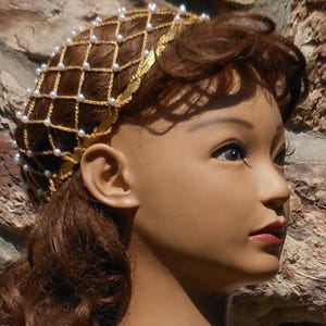 Op de afbeelding: Een gouden draad haarnet met witte parels, gedragen op een mannequinhoofd met bruin haar.